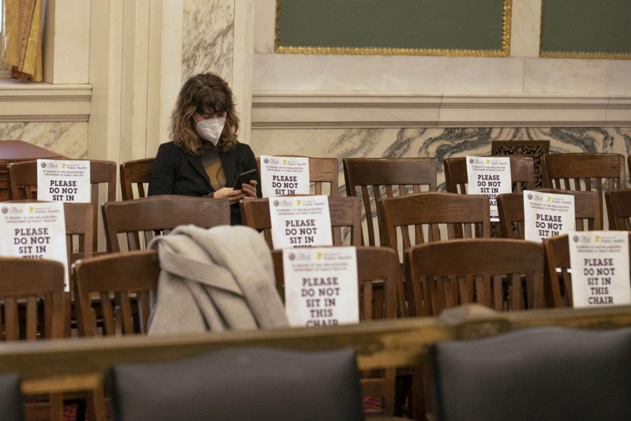 A person wearing a mask sits among signs that promote social distancing with seating at City Hall in January.