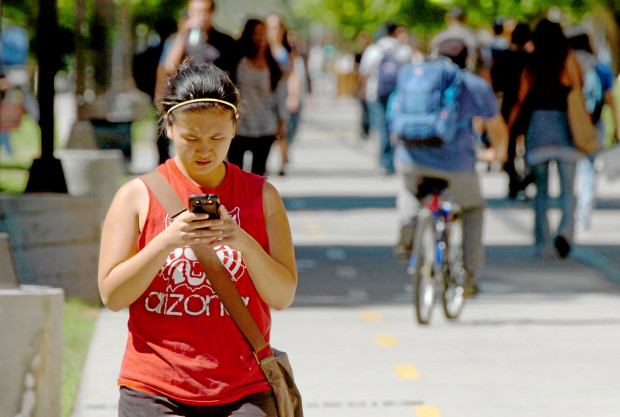 A student makes her way down the Jacaranda walk/bike path through campus while using her smart phone at Cal State University Northridge in Northridge, CA. Wednesday September 24, 2014. Women college students spend an average of 10 hours a day on their cellphones and men college students spend nearly eight, with excessive use posing potential risks for academic performance, according to a recent Baylor University study on cell phone activity published in the Journal of Behavioral Addictions. The study says about 60 percent of college students admit they may be addicted to their cell phone, and some indicated they get agitated when it is not in sight.   (Thomas R. Cordova-Daily Breeze/Press-Telegram)