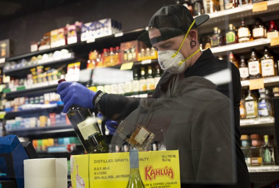 Protecting employees became a priority for business as the pandemic took hold. Here, Dustin Anderson wears a face mask and gloves, and stands behind a plastic barrier, while working at the Cedar Mill Liquor Store in Portland last March.