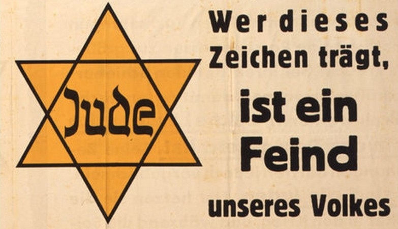 A yellow badge in the shape of the Star of David, used by the Nazi German regime to identify Jewish people.
The text reads:
